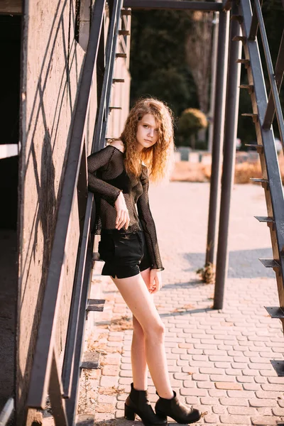 Red-haired girl in a black dress near a dark textured wall — Stock Photo, Image