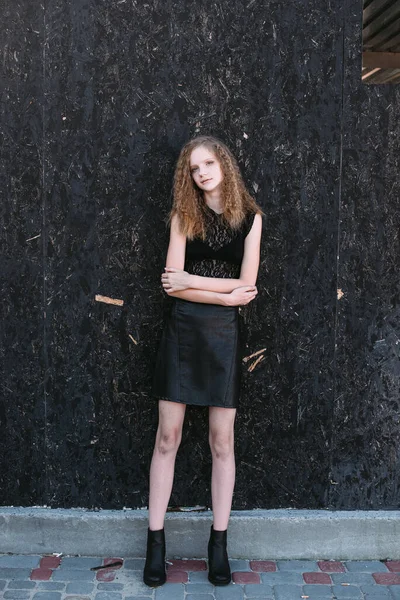 Red-haired girl in a black dress near a dark textured wall — Stock Photo, Image