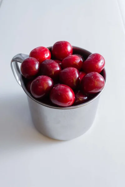 Cerejas doces em uma caneca de aço em um fundo de papel branco — Fotografia de Stock