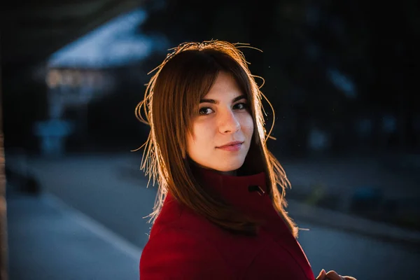 Young beautiful girl in a red coat and hat in the evening in the city — Stock Photo, Image