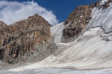 Karlı dağ manzarası güneşli bir havada kayalık yamaçtan geçer. 