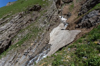 Güneşli baharda, kayalık dağlarda, buzun altında akan hızlı dağ deresinin resimsel görüntüsü. 