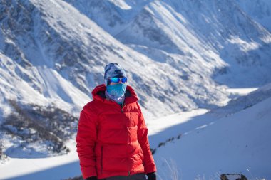 Sıcak, sportif giysiler içinde turist güneşli kış gününde karlı dağlarda dikiliyor. 