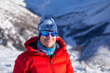 Sıcak, sportif giysiler içinde turist güneşli kış gününde karlı dağlarda dikiliyor. 