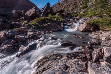 Güneşli baharda kayalık dağlarda akan hızlı dağ deresinin resimsel görüntüsü 