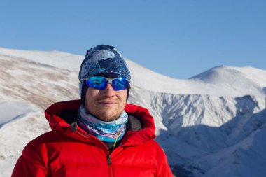 Sıcak, sportif giysiler içinde turist güneşli kış gününde karlı dağlarda dikiliyor. 