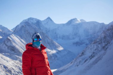 Sıcak, sportif giysiler içinde turist güneşli kış gününde karlı dağlarda dikiliyor. 