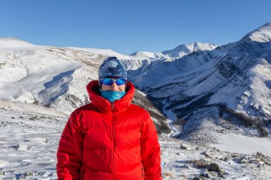 Sıcak, sportif giysiler içinde turist güneşli kış gününde karlı dağlarda dikiliyor. 