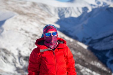 Sıcak, sportif giysiler içinde gezgin güneşli kış gününde karlı dağlarda yürüyüş yapıyor. 