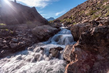 Güneşli baharda kayalık dağlarda akan hızlı dağ deresinin resimsel görüntüsü 