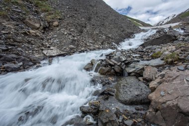 Güneşli baharda kayalık dağlarda akan hızlı dağ nehrinin resimsel manzarası 