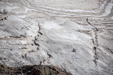 Karlı dağlarda yürüyüş yapan gezginler güneşli bir havada kayalık yamaçtan geçiyorlar. 
