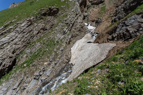 Güneşli baharda, kayalık dağlarda, buzun altında akan hızlı dağ deresinin resimsel görüntüsü. 