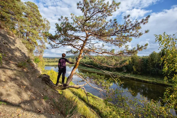 Nehir kenarındaki bir kayanın üzerinde, doğa geçmişi olan genç bir adam. manzara, doğaya yolculuk