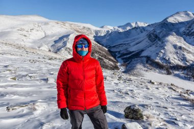 Sıcak, sportif giysiler içinde turist güneşli kış gününde karlı dağlarda dikiliyor. 