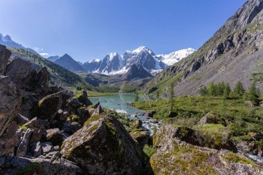 Mavi nehir manzarası ve Tien Shan dağlarının karlı tepeleri baharda güneşli bir günde. 