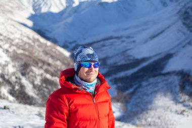 Sıcak, sportif giysiler içinde turist güneşli kış gününde karlı dağlarda dikiliyor. 