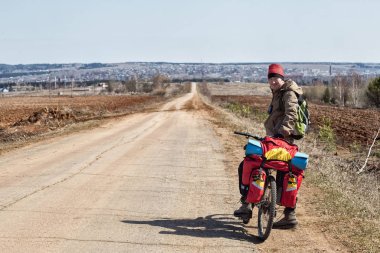 Genç erkek bisikletçi güneşli bahar gününde ormanın yakınındaki toprak yolda bisiklet sürüyor. 