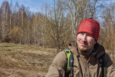 Kırmızı şapkalı ve sıcak elbiseli bir adam güneşli bir günde ormanda yürüyor. 