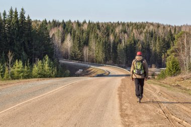 Genç erkek gezgin güneşli bahar gününde ormanın yanındaki toprak yolda yürüyor. 