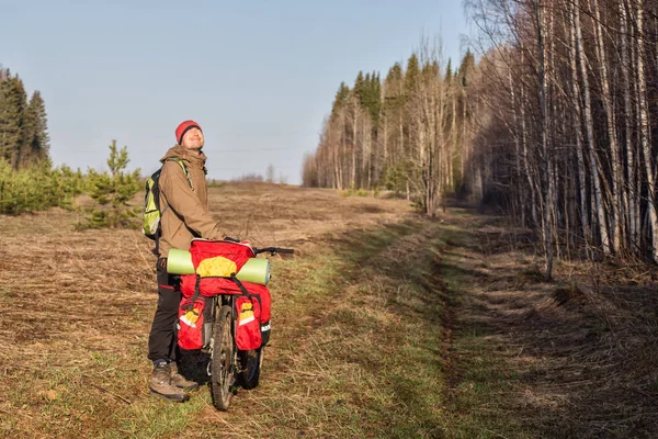 Genç erkek bisikletçi güneşli bahar gününde ormanın yakınında bisiklet sürüyor. 