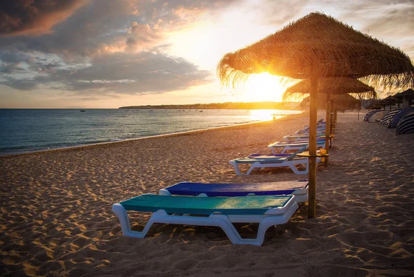 日落灯光下的沙滩稻草伞和甲板椅 — 图库照片