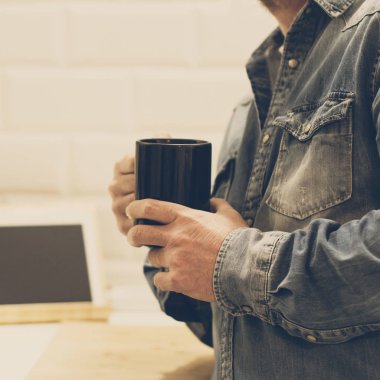 Elinde siyah bir kupa olan adam