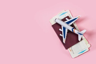 Pembe arka planda pasaportlu ve biniş kartı olan bir oyuncak uçak