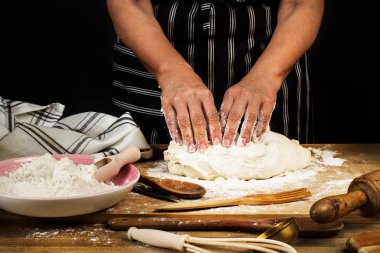 Ahşap bir masada hamur yoğuran kadın.