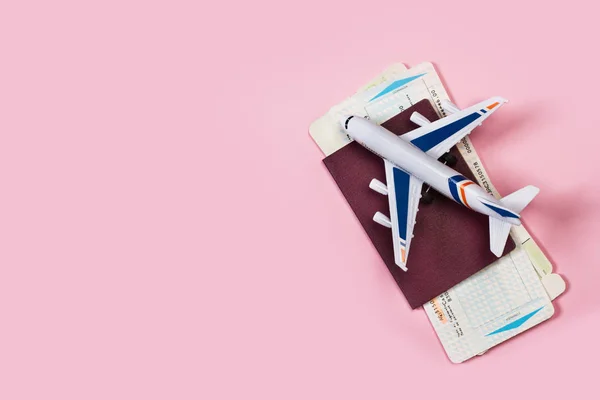 Pembe arka planda pasaportlu ve biniş kartı olan bir oyuncak uçak