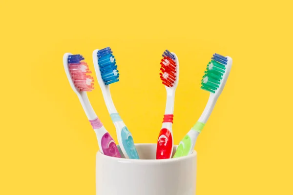 Plastic colored toothbrushes in a ceramic glass on a yellow background