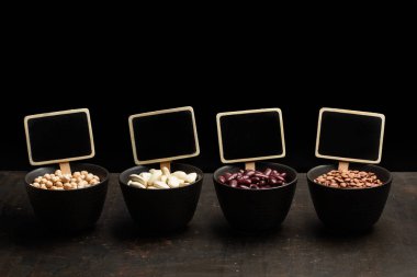 Koyu bir arka plan üzerinde siyah kaselerde fasulye, mercimek ve nohut