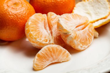 Beyaz bir tabak üzerinde segmentlerde soyulmuş mandalina