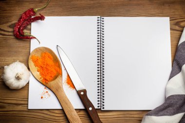 Tahta bir masanın üzerinde bir defter üzerinde sarımsak ve kırmızı biber ile tahta bir kaşık