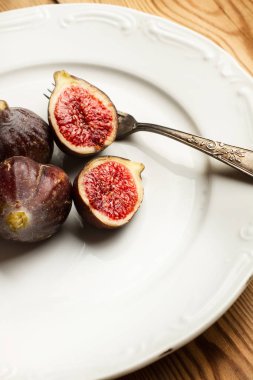 Çatalile beyaz bir tabak üzerinde incir ve iki yarım incir