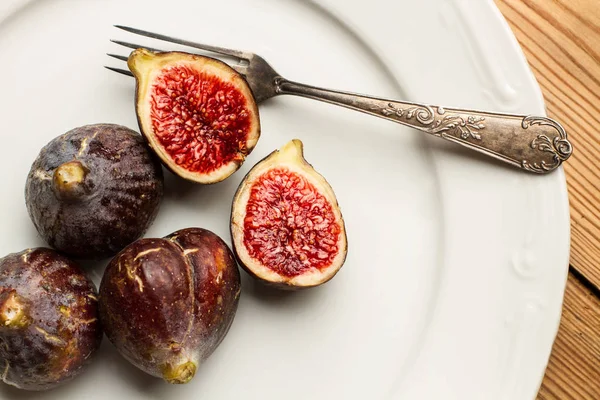 Çatalile beyaz bir tabak üzerinde incir ve iki yarım incir