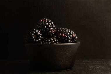 Siyah bir kasede siyah bir arka planda böğürtlen