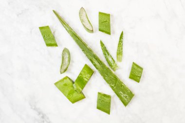 Aloe vera yaprağı parçaları mermer bir masanın üstünde, en üstte.