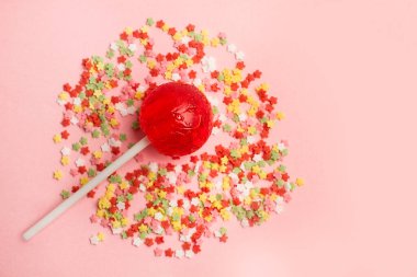 Pembe arka planda kırmızı bir lolipop ve renkli yıldız sürükleniyor.