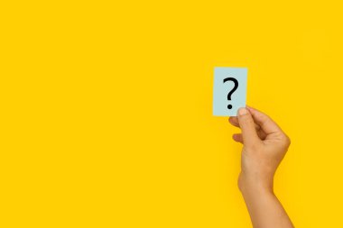 Woman hand holding a paper with a question sign on a yellow background clipart