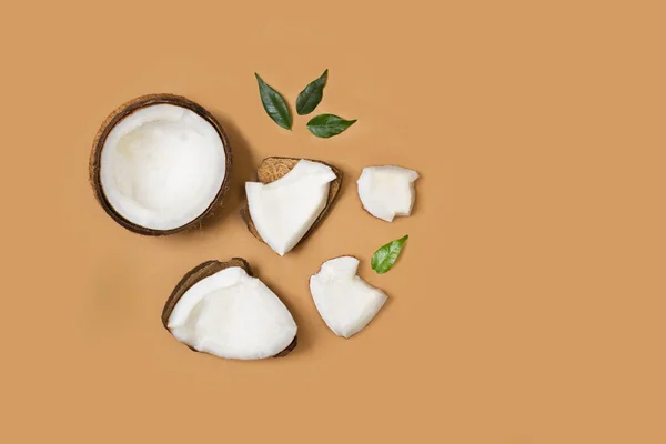Halved coconut with pieces of coconut on a brown background in a top view