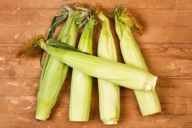 Tahta bir masanın üstünde yaprakları olan mısır.