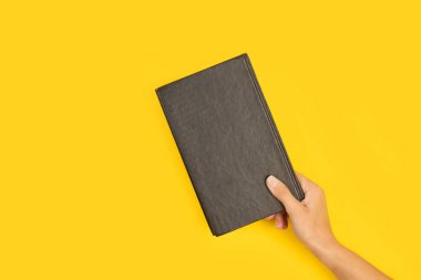 Sarı arka planda siyah bir kitabı tutan bir kadın.