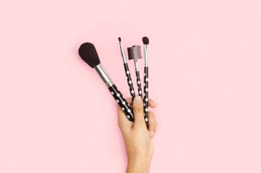 Pembe arka planda el ele tutuşan kadın makyaj fırçaları