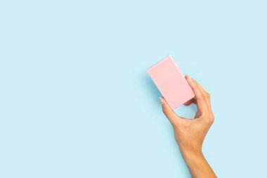 Açık mavi arka planda pembe sabun tutan bir kadın.