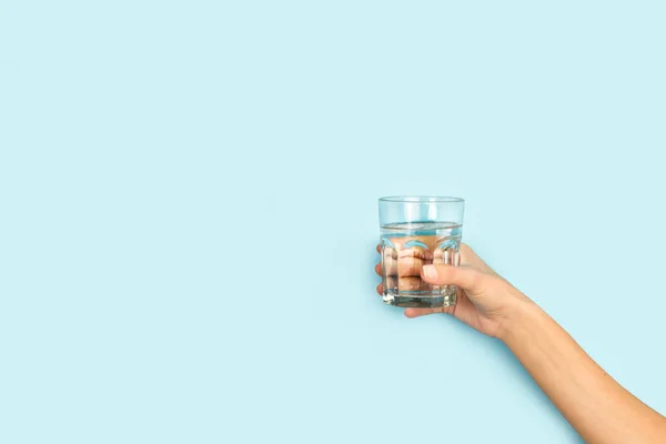 stock image Woman hand holding a glass of water on a light blue background