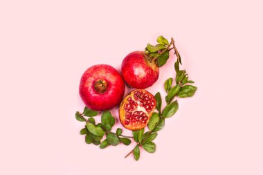 Pembe arkaplanda dalları ve yaprakları olan bir nar ve üst görünümde kopyalama alanı