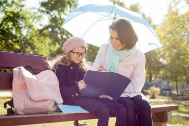 Anne ve kızı birlikte şehir parkta bir bankta kız gözlük okuma anne Öğrenci yarıyıl not defteri ve okul hayatı hakkında görüşmeler dinlenme.