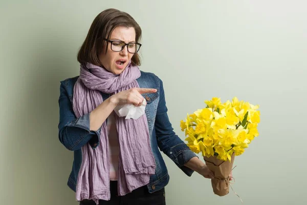 Spring allergy to pollen. Woman with bouquet of yellow flowers is going to sneeze. Background green matte wall