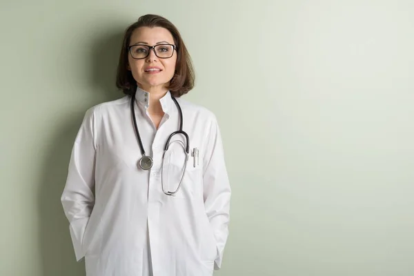 正中年女医生戴眼镜背景绿色墙壁在诊所里 — 图库照片